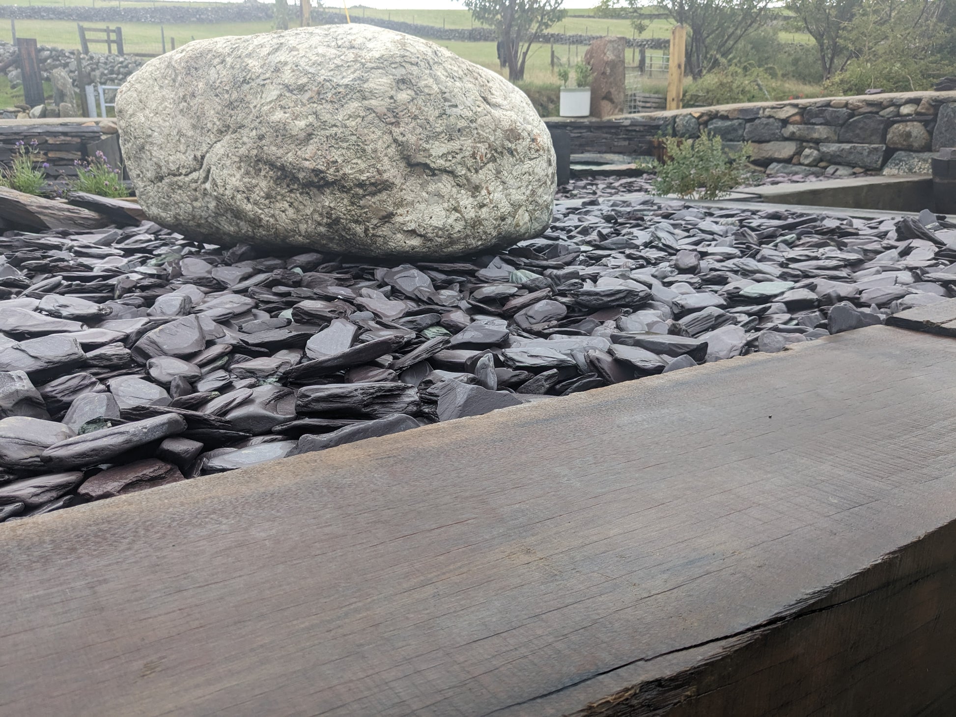 Large glacial boulder on a bed of blue slate paddlestones with a wooden railway sleeper in the foreground