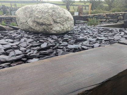 Large glacial boulder on a bed of blue slate paddlestones with a wooden railway sleeper in the foreground